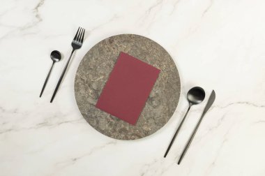 Kahverengi mermer plaka, siyah çatal bıçak takımı ve beyaz mermer arka planda koyu kırmızı kart. Yemek sunumu, taş tepsi. Tablo ayarı, kopyalama alanı, düz uzanma.