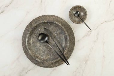 Kahverengi mermer tepsi, tabak, kase ve siyah çatal bıçak takımları beyaz mermer arka planda. Yemek sunumu, tabaklar, taş tepsi. Uzayı kopyala, düz yat.