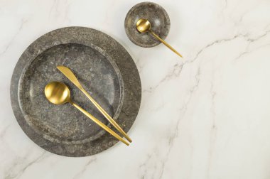 Kahverengi mermer tepsi, tabak, kase ve beyaz mermer arka planda altın çatal bıçak. Yemek sunumu, tabaklar, taş tepsi. Uzayı kopyala, düz yat.