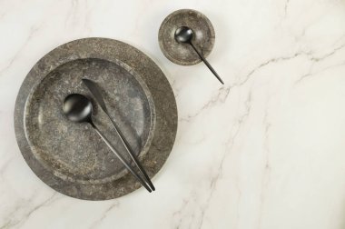 Kahverengi mermer tepsi, tabak, kase ve siyah çatal bıçak takımları beyaz mermer arka planda. Yemek sunumu, tabaklar, taş tepsi. Uzayı kopyala, düz yat.