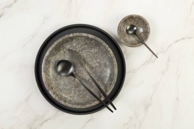 Siyah plaka, kahverengi mermer plaka, kâse ve beyaz mermer arka planda siyah çatal bıçak. Yemek sunumu, bulaşıklar, siyah tepsi. Uzayı kopyala, düz yat.