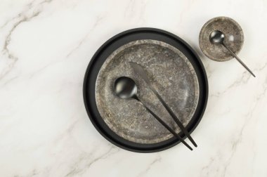 Siyah plaka, kahverengi mermer plaka, kâse ve beyaz mermer arka planda siyah çatal bıçak. Yemek sunumu, bulaşıklar, siyah tepsi. Uzayı kopyala, düz yat.