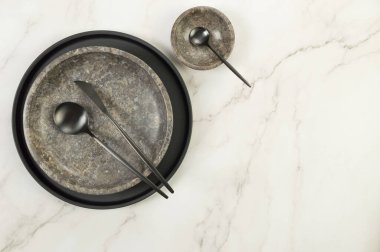 Siyah plaka, kahverengi mermer plaka, kâse ve beyaz mermer arka planda siyah çatal bıçak. Yemek sunumu, bulaşıklar, siyah tepsi. Uzayı kopyala, düz yat.