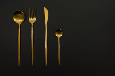 Siyah arkaplandaki altın çatal bıçak takımının en üst görüntüsü. Bıçak, çatal, kaşık ve tatlı kaşığı. Uzayı kopyala, düz yat.
