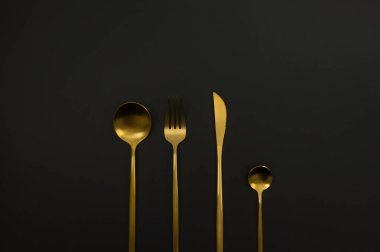Siyah arkaplandaki altın çatal bıçak takımının en üst görüntüsü. Bıçak, çatal, kaşık ve tatlı kaşığı. Uzayı kopyala, düz yat.