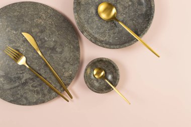 Pembe arka planda kahverengi mermer tepsi, tabak, kase ve altın çatal bıçak. Yemek sunumu, tabaklar, taş tepsi. Uzayı kopyala, düz yat.