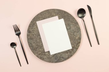 Kahverengi mermer plaka, pembe arka planda siyah çatal bıçak. Beyaz ve pembe kartlar. Yemek sunumu, taş tepsi. Tablo ayarı, kopyalama alanı, düz uzanma.