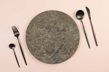 Kahverengi mermer plaka, pembe arka planda siyah çatal bıçak. Yemek sunumu, taş tepsi. Tablo ayarı, kopyalama alanı, düz uzanma.