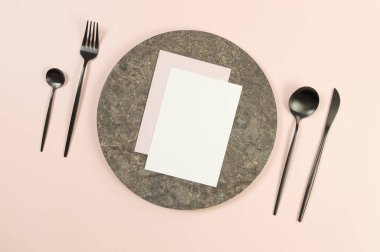Kahverengi mermer plaka, pembe arka planda siyah çatal bıçak. Beyaz ve pembe kartlar. Yemek sunumu, taş tepsi. Tablo ayarı, kopyalama alanı, düz uzanma.