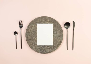 Kahverengi mermer plaka, siyah çatal bıçak takımı ve pembe arka planda beyaz kart. Yemek sunumu, taş tepsi. Tablo ayarı, kopyalama alanı, düz uzanma.