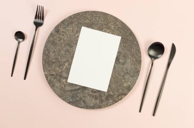 Kahverengi mermer plaka, siyah çatal bıçak takımı ve pembe arka planda beyaz kart. Yemek sunumu, taş tepsi. Tablo ayarı, kopyalama alanı, düz uzanma.