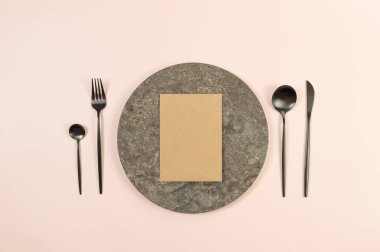 Kahverengi mermer plaka, siyah çatal bıçak takımı ve pembe arka planda kahverengi kraft kartı. Yemek sunumu, taş tepsi. Tablo ayarı, kopyalama alanı, düz uzanma.