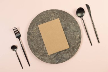 Kahverengi mermer plaka, siyah çatal bıçak takımı ve pembe arka planda kahverengi kraft kartı. Yemek sunumu, taş tepsi. Tablo ayarı, kopyalama alanı, düz uzanma.
