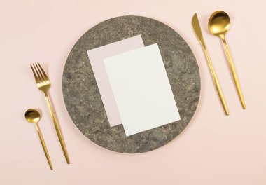 Kahverengi mermer plakanın üst manzarası, pembe arka planda altın çatal bıçak takımı. Beyaz ve pembe kartlar. Yemek sunumu, taş tepsi. Tablo ayarı, kopyalama alanı, düz uzanma.