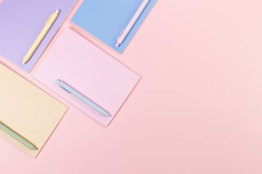 Pembe, mor, mavi ve bej renkli defterlerin pembe arka planda üst görüntüsü. Renkli kalemler, okul, ofis kağıdı. Düz yat, boşluğu kopyala.