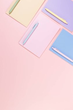 Pembe, mor, mavi ve bej renkli defterlerin pembe arka planda üst görüntüsü. Renkli kalemler, okul, ofis kağıdı. Düz yat, boşluğu kopyala.