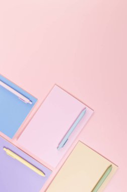 Pembe, mor, mavi ve bej renkli defterlerin pembe arka planda üst görüntüsü. Renkli kalemler, okul, ofis kağıdı. Düz yat, boşluğu kopyala.