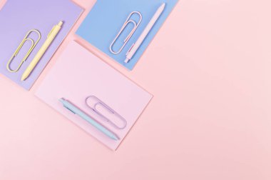 Pembe, mor ve mavi arkaplanlı defterlerin üst görüntüsü. Pembe, sarı ve mavi kalemler, ataçlar, okul, ofis kağıdı. Düz yat, boşluğu kopyala.