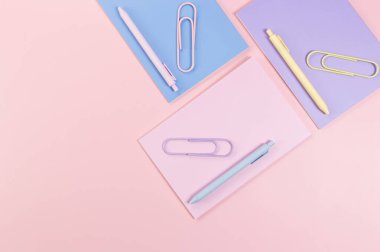 Pembe, mor ve mavi arkaplanlı defterlerin üst görüntüsü. Pembe, sarı ve mavi kalemler, ataçlar, okul, ofis kağıdı. Düz yat, boşluğu kopyala.