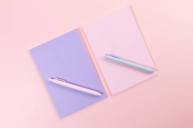 Pembe arka plandaki pembe ve mor defterlerin üst görüntüsü. Pembe ve mavi kalemler, okul, ofis kağıdı. Düz yat, boşluğu kopyala.