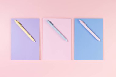 Pembe, mor ve mavi arkaplanlı defterlerin üst görüntüsü. Pembe, sarı ve mavi kalemler, okul, ofis kağıdı. Düz yat, boşluğu kopyala.