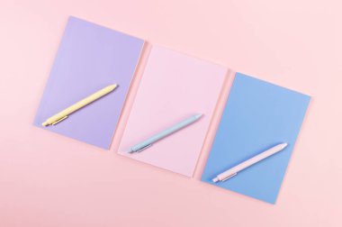 Pembe, mor ve mavi arkaplanlı defterlerin üst görüntüsü. Pembe, sarı ve mavi kalemler, okul, ofis kağıdı. Düz yat, boşluğu kopyala.