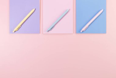 Pembe, mor ve mavi arkaplanlı defterlerin üst görüntüsü. Pembe, sarı ve mavi kalemler, okul, ofis kağıdı. Düz yat, boşluğu kopyala.