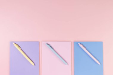 Pembe, mor ve mavi arkaplanlı defterlerin üst görüntüsü. Pembe, sarı ve mavi kalemler, okul, ofis kağıdı. Düz yat, boşluğu kopyala.
