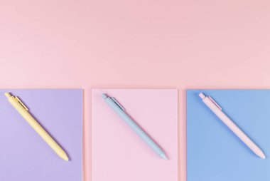 Pembe, mor ve mavi arkaplanlı defterlerin üst görüntüsü. Pembe, sarı ve mavi kalemler, okul, ofis kağıdı. Düz yat, boşluğu kopyala.