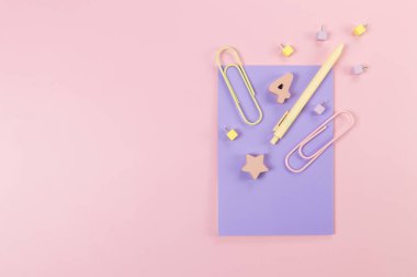 Pembe arka planda mor defterin üst görüntüsü. Ataç, kalem, numara, şekil ve iğne. Okul, ofis duvar kağıdı. Düz yat, boşluğu kopyala.