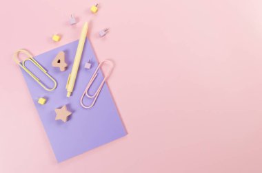 Pembe arka planda mor defterin üst görüntüsü. Ataç, kalem, numara, şekil ve iğne. Okul, ofis duvar kağıdı. Düz yat, boşluğu kopyala.