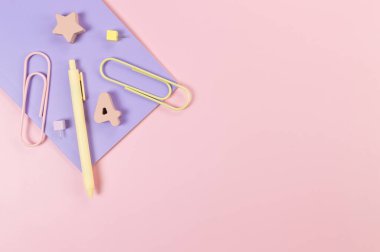 Pembe arka planda mor defterin üst görüntüsü. Ataç, kalem, numara, şekil ve iğne. Okul, ofis duvar kağıdı. Düz yat, boşluğu kopyala.