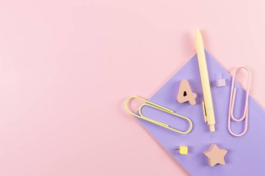 Pembe arka planda mor defterin üst görüntüsü. Ataç, kalem, numara, şekil ve iğne. Okul, ofis duvar kağıdı. Düz yat, boşluğu kopyala.