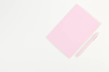 Pembe defterin üst görüntüsü, beyaz arka planda pembe kalem. Okul, ofis duvar kağıdı. Düz yat, boşluğu kopyala.