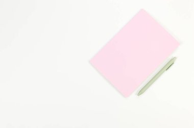 Pembe defterin üst görüntüsü, beyaz arka planda yeşil kalem. Okul, ofis duvar kağıdı. Düz yat, boşluğu kopyala.
