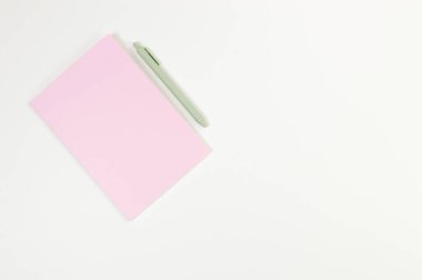 Pembe defterin üst görüntüsü, beyaz arka planda yeşil kalem. Okul, ofis duvar kağıdı. Düz yat, boşluğu kopyala.