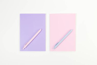 Pembe ve mor defterlerin üst görüntüsü, beyaz arka planda pembe ve mavi kalemler. Okul, ofis duvar kağıdı. Düz yat, boşluğu kopyala.