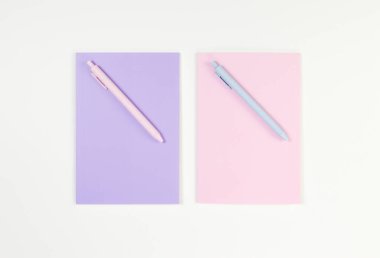 Pembe ve mor defterlerin üst görüntüsü, beyaz arka planda pembe ve mavi kalemler. Okul, ofis duvar kağıdı. Düz yat, boşluğu kopyala.