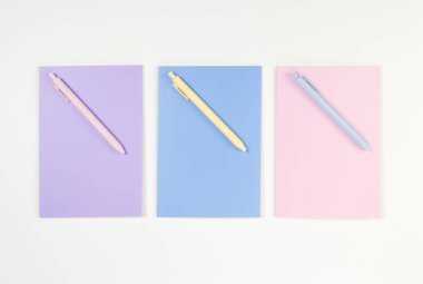 Beyaz arka planda pembe, mor ve mavi defterlerin üst görüntüsü. Pembe, sarı ve mavi kalemler, okul, ofis kağıdı. Düz yat, boşluğu kopyala.