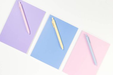 Beyaz arka planda pembe, mor ve mavi defterlerin üst görüntüsü. Pembe, sarı ve mavi kalemler, okul, ofis kağıdı. Düz yat, boşluğu kopyala.