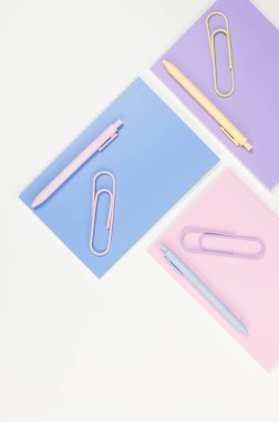 Beyaz arka planda pembe, mor ve mavi defterlerin üst görüntüsü. Pembe, sarı ve mavi kalemler, ataçlar, okul, ofis kağıdı. Düz yat, boşluğu kopyala.
