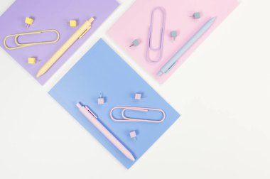 Beyaz arka planda pembe, mor ve mavi defterlerin üst görüntüsü. Renkli kalemler, ataçlar, raptiyeler, okul, ofis kağıdı. Düz yat, boşluğu kopyala.