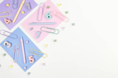 Beyaz arka planda pembe, mor ve mavi defterlerin üst görüntüsü. Renkli kalemler, ataçlar, numaralar ve iğneler. Okul, ofis duvar kağıdı. Düz yat, boşluğu kopyala.