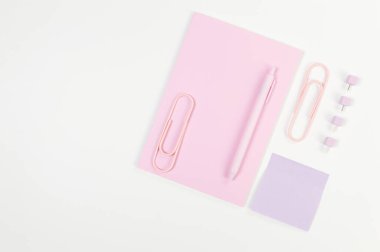 Beyaz arka planda pembe defterin üst görüntüsü. Yapışkan not, ataç, kalem ve iğne. Okul, ofis duvar kağıdı. Düz yat, boşluğu kopyala.