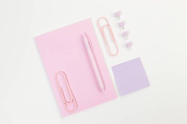 Beyaz arka planda pembe defterin üst görüntüsü. Yapışkan not, ataç, kalem ve iğne. Okul, ofis duvar kağıdı. Düz yat, boşluğu kopyala.