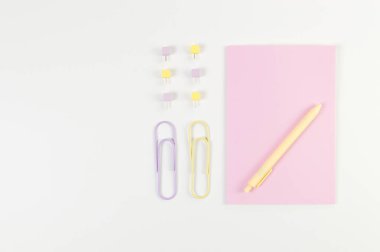 Beyaz arka planda pembe defterin üst görüntüsü. Ataç, kalem ve raptiye. Okul, ofis duvar kağıdı. Düz yat, boşluğu kopyala.