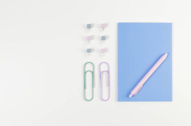 Beyaz arkaplanda mavi defterin üst görüntüsü. Ataç, kalem ve raptiye. Okul, ofis duvar kağıdı. Düz yat, boşluğu kopyala.