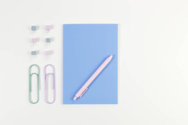 Beyaz arkaplanda mavi defterin üst görüntüsü. Ataç, kalem ve raptiye. Okul, ofis duvar kağıdı. Düz yat, boşluğu kopyala.