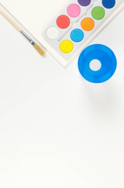 Beyaz arka planda suluboya, boya fırçası, kağıt ve su kabının üst görüntüsü. Resim, sanat, kopyalama alanı, düzlük.