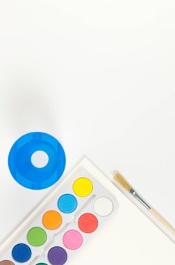 Beyaz arka planda suluboya, boya fırçası, kağıt ve su kabının üst görüntüsü. Resim, sanat, kopyalama alanı, düzlük.